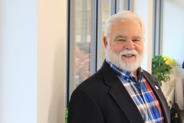 male executive with white beard wearing a black jacket and plaid shirt