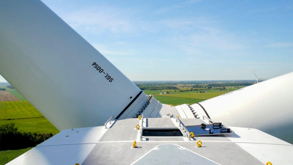 Photograph of a wind turbine from the top of the structure--showing the blades and sweeping farmland ahead.