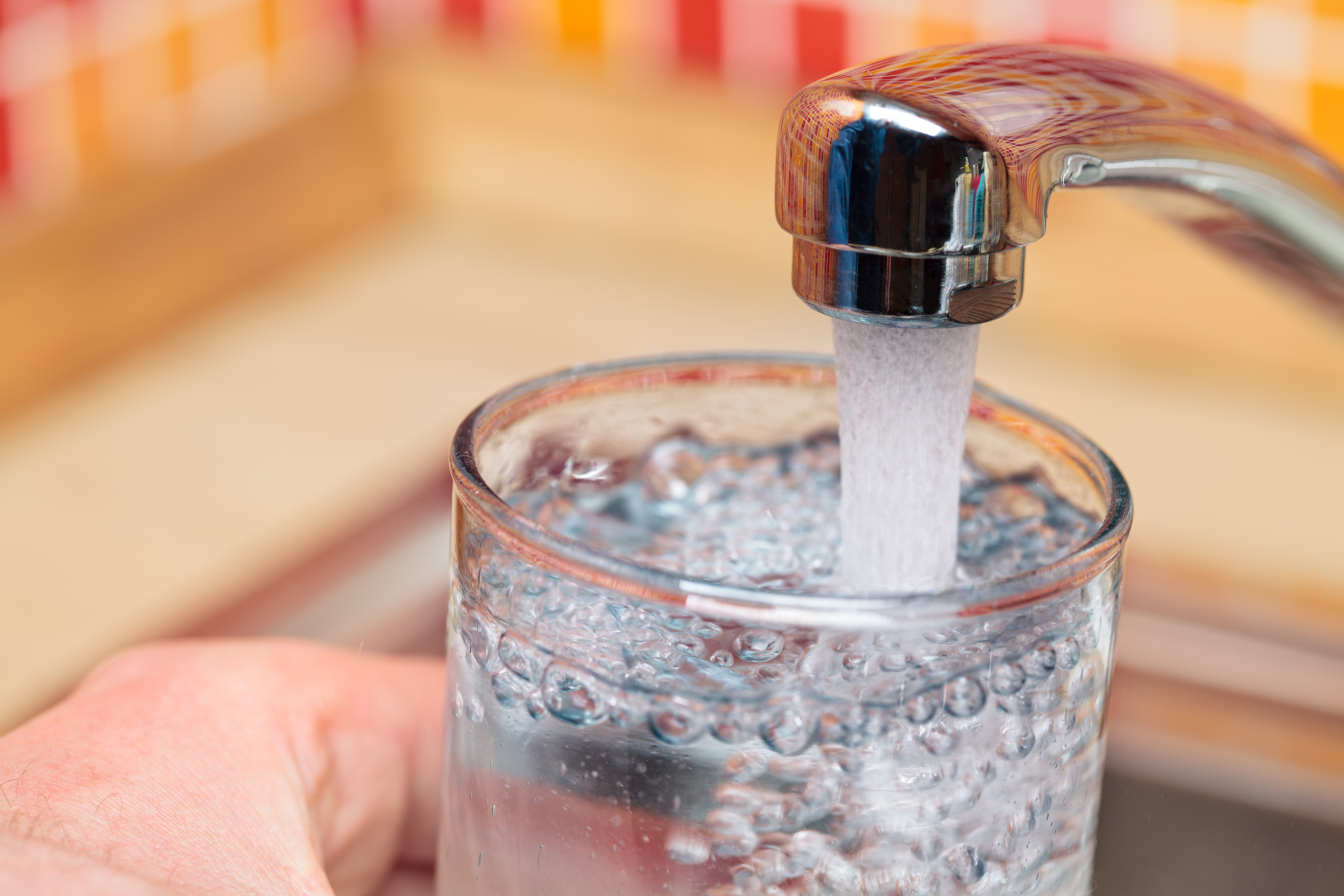 A hand holds a clear glass of water that is filled by a tap on a sink.