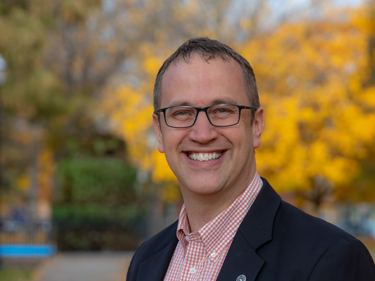 male executive wearing a black jacket and red checkered shirt