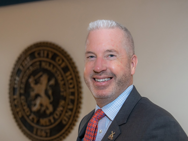 male executive wearing a black jacket, blue shirt, and orange tie