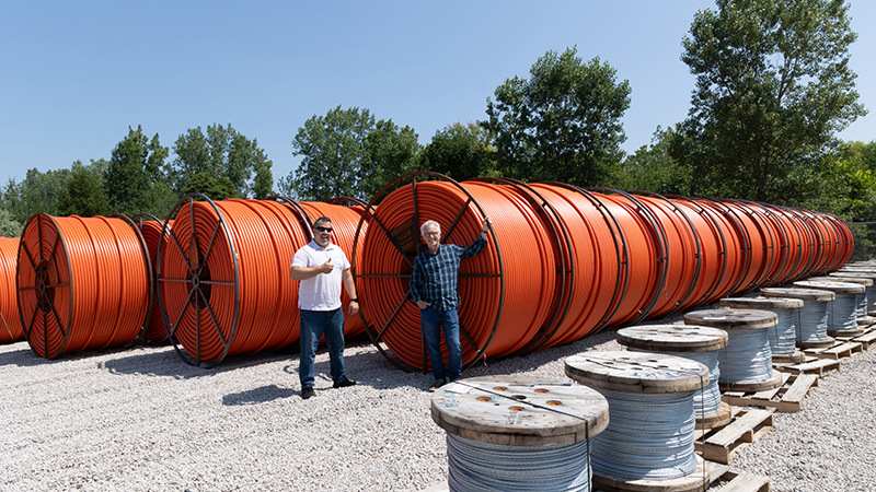 two men standing in front of giant spools of orange conduit and grey wire
