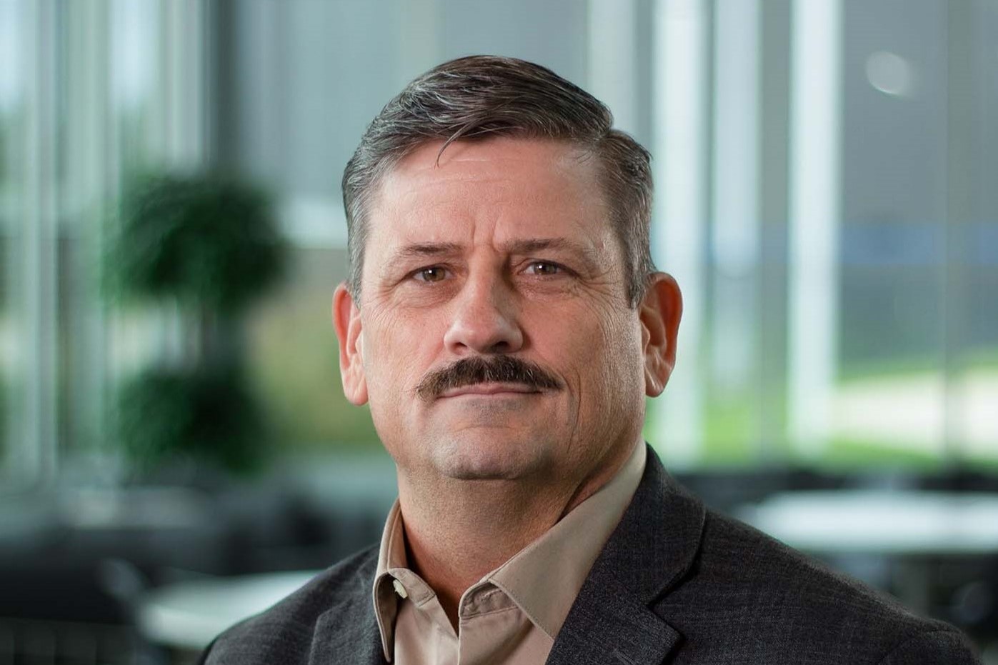 male executive with a moustache wearing a black jacket and brown shirt