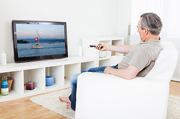 an older man is watching tv. he is pointing the remote at the screen
