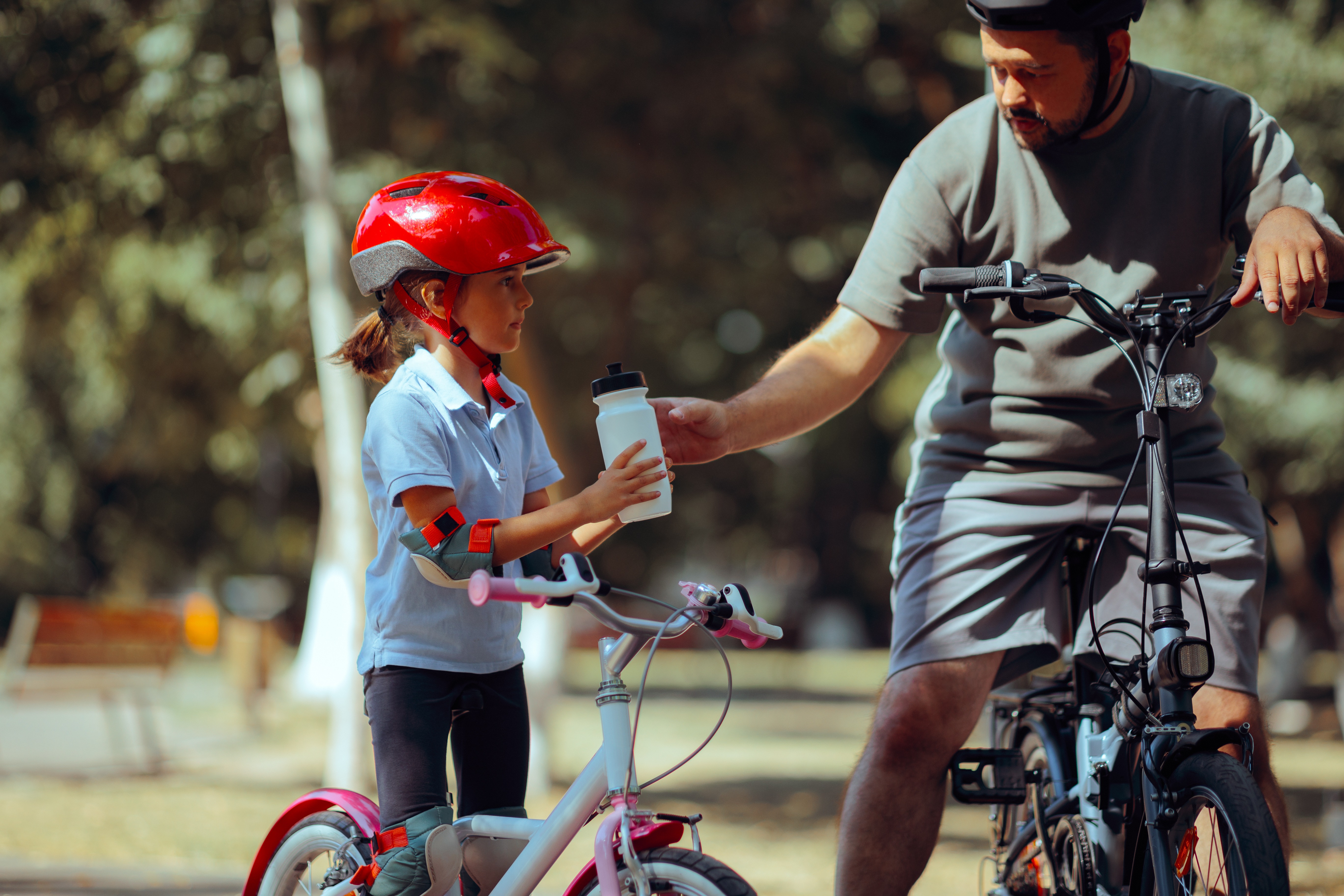 Girl and dad biking. Dad gives her a drink of water